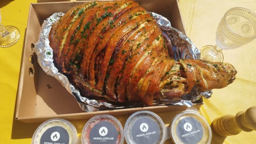 Pernil de cerdo dorado en su fuente, con potes de salsas